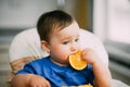 A little girl in a blue t-shirt sitting in a child seat and eating an orange Royalty Free Stock Photo