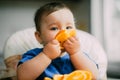 A little girl in a blue t-shirt sitting in a child seat and eating an orange Royalty Free Stock Photo