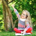 Little girl with a book in a park wearing glasses pointing at co Royalty Free Stock Photo