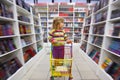 Little girl in bookshop, with cart for goods Royalty Free Stock Photo