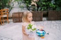 Little girl with a bouquet of flowers stands in the courtyard of the house and looks away
