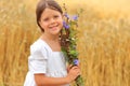 Little girl with a bouquet of wildflowers in her hands in a wheat field.