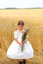 Little girl with a bouquet of wildflowers in her hands in a wheat field.