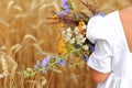 Little girl with a bouquet of wildflowers in her hands in a wheat field.