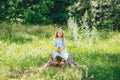 Little girl with bouquet of yellow wild flowers sitting on wooden stump and dreaming in sunny day Royalty Free Stock Photo