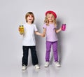 Little girl and boy in colorful casual clothes. Smiling, holding hands, yellow and pink cocktail bottles. Posing isolated on white Royalty Free Stock Photo