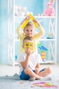 A little girl with a boy is sitting on the floor and holding a house of colored paper. Royalty Free Stock Photo