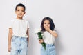 little girl and boy stand on a light background with a bouquet of flowers and the girl closes her mouth with her hand in Royalty Free Stock Photo