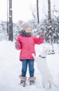 Little girl in a bright jacket plays in the winter snowy forest with her dog
