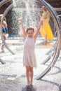 Little girl in a bright sundress rejoices drops of the city fountain