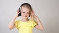 A little girl in a bright yellow dress listens to music with headphones. The girl puts the headphones on her head.