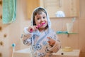 A little girl is brushing her teeth. A child in a bathrobe in the bathroom washes.