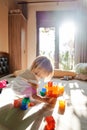 Little girl builds a house from Lego blocks while squatting on the bed. Side view Royalty Free Stock Photo