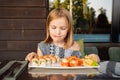 little girl in cafe, restaurant, country house smiles and licks looks Asian Japanese sushi rolls