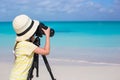 Little girl with camera on a tripod at white sandy beach Royalty Free Stock Photo