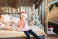 Little girl in the cap of Santa Claus is waiting for the New Year on the bed. Girl on Christmas with gifts in the bedroom in the s Royalty Free Stock Photo