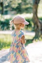 Little girl in a cap walks along a path in a sunny garden. Back view