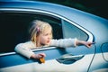 Little girl in the car shows something. Little girl sitting in the car. Adorable little girl looking out of car window.