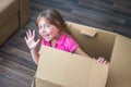 A little girl is in a cardboard box. Baby moves to a new apartment. Beautiful kid sits in a mail box. The child plays funny.