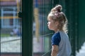 A little girl carefully looks over the fence at the children`s playground. Concept: the desire to play sports, the limitations of Royalty Free Stock Photo