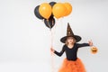 A little girl in a carnival witch costume and hat holding a basket for treats and orange and black balloons scares Royalty Free Stock Photo