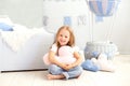 A little girl in casual clothes holds a cloud pillow against the background of a decorative balloon. The child plays in children r