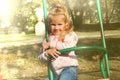 Little girl child in autumn clothes in  park swinging on swing and laughing, retro effect sun glare Royalty Free Stock Photo