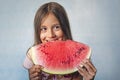 A little girl child bites a large piece of watermelon on a blue background. Happy toddler eating melon Royalty Free Stock Photo