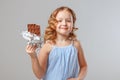 Little girl child blonde holds a bitten bar of chocolate in her hands. Gray background, studio, portrait Royalty Free Stock Photo