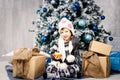 Little girl child of five years sitting on the floor near Christmas tree decorated with toys, balls. In the hands holds an orange Royalty Free Stock Photo