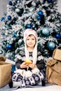 Little girl child of five years sitting on the floor near Christmas tree decorated with toys, balls. In the hands holds Royalty Free Stock Photo