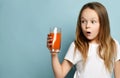 Little girl child kid drinking carrot orange juice surprised in white copy space blank t-shirt on light blue background Royalty Free Stock Photo