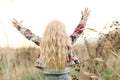 Little girl child with long blondy wavy hair. Happy child raise up hands at sunset at nature. Beautiful warm summer evening. Kids