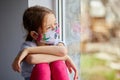 Little girl, child in mask sits on windows, coronavirus quarantine