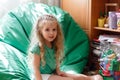 Little girl child Portrait in children& x27;s room with Toys and clutter. 5 Years happy smiling kid girl Sit on green beanbag Royalty Free Stock Photo