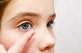 Little girl child putting contact lens into her eye closeup