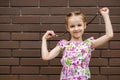 A little girl child stands against a brick wall and playfully holds her pigtails Royalty Free Stock Photo