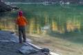 A child, in warm clothes and a red cap throws stones into the water from the sandy shore Royalty Free Stock Photo