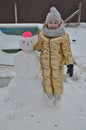Little girl child in winter sculpts a snowman from the snow.