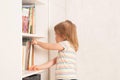 Little girl chooses a book in a bookcase at home. Royalty Free Stock Photo