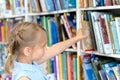 Little girl chooses, takes book with fairy tales from shelf in children`s library.Special reading kids room.Many shelves with Royalty Free Stock Photo