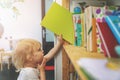 Little girl choosing and taking book from shelf to read