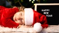 A little girl in a Christmas costume and Santa Claus hat is sleeping under the tree waiting for a miracle Royalty Free Stock Photo