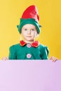 Little girl in a Christmas elf costume on a yellow background. Beautiful child in a red hat with bells. Copy space. Royalty Free Stock Photo