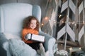 Little girl with a Christmas gift sitting in a comfortable chair Royalty Free Stock Photo