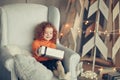 little girl with a Christmas gift sitting in a comfortable chair Royalty Free Stock Photo