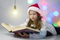 Little girl in a Christmas hat of Santa Claus reads in a book. Royalty Free Stock Photo