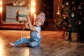 A little girl in the Christmas living room sits near the Christmas tree and opens gifts. Royalty Free Stock Photo