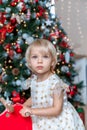 little girl Christmas tree. Blonde 2 years old in a dress sits on a wooden red horse in a room decorated for christmas Royalty Free Stock Photo