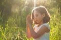 Little Girl closed her eyes, praying in a field during beautiful sunset. Hands folded in prayer concept for faith Royalty Free Stock Photo